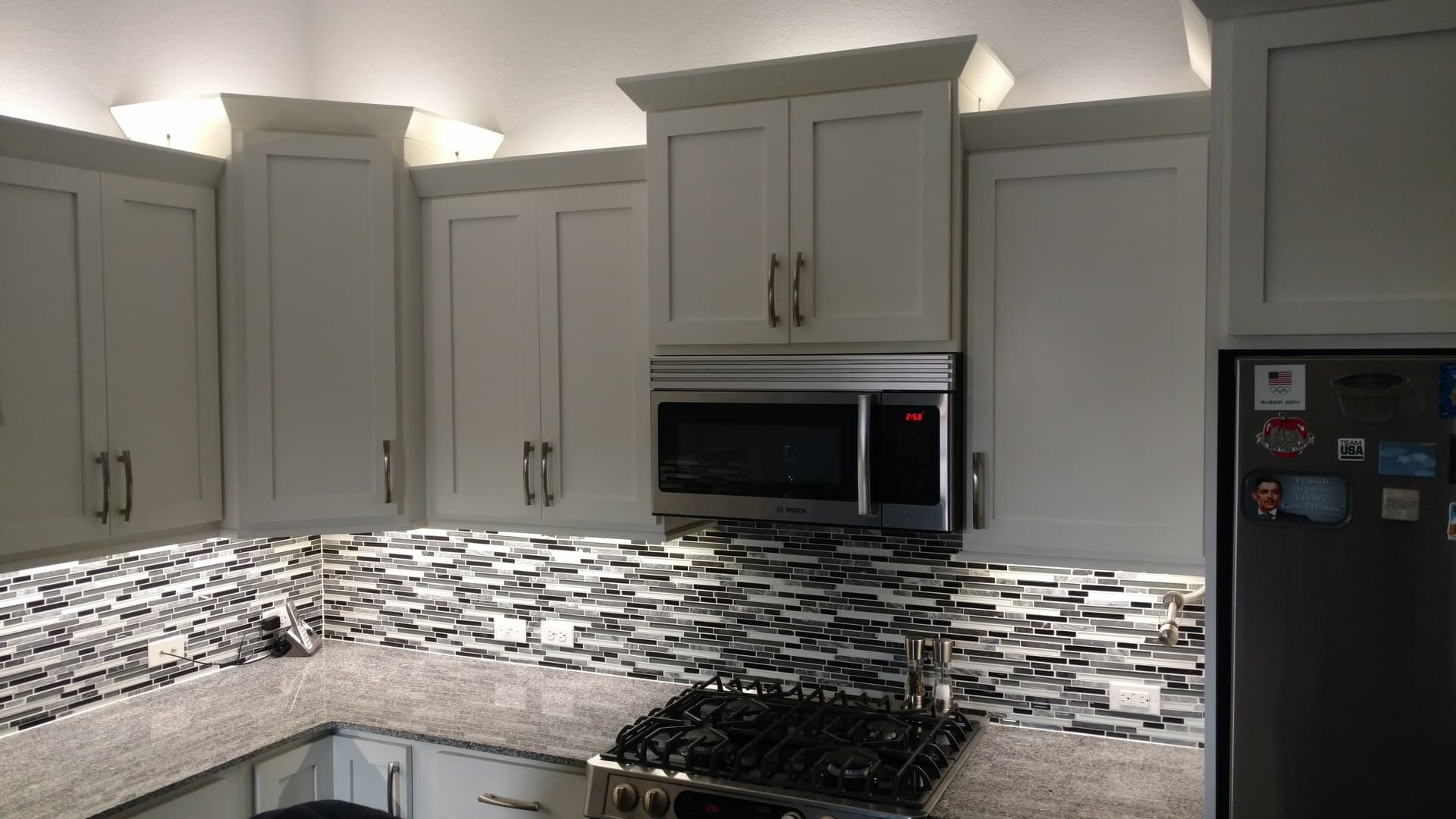Kitchen with under-cabinet and above-cabinet lighting, white shaker cabinets and mosaic backsplash